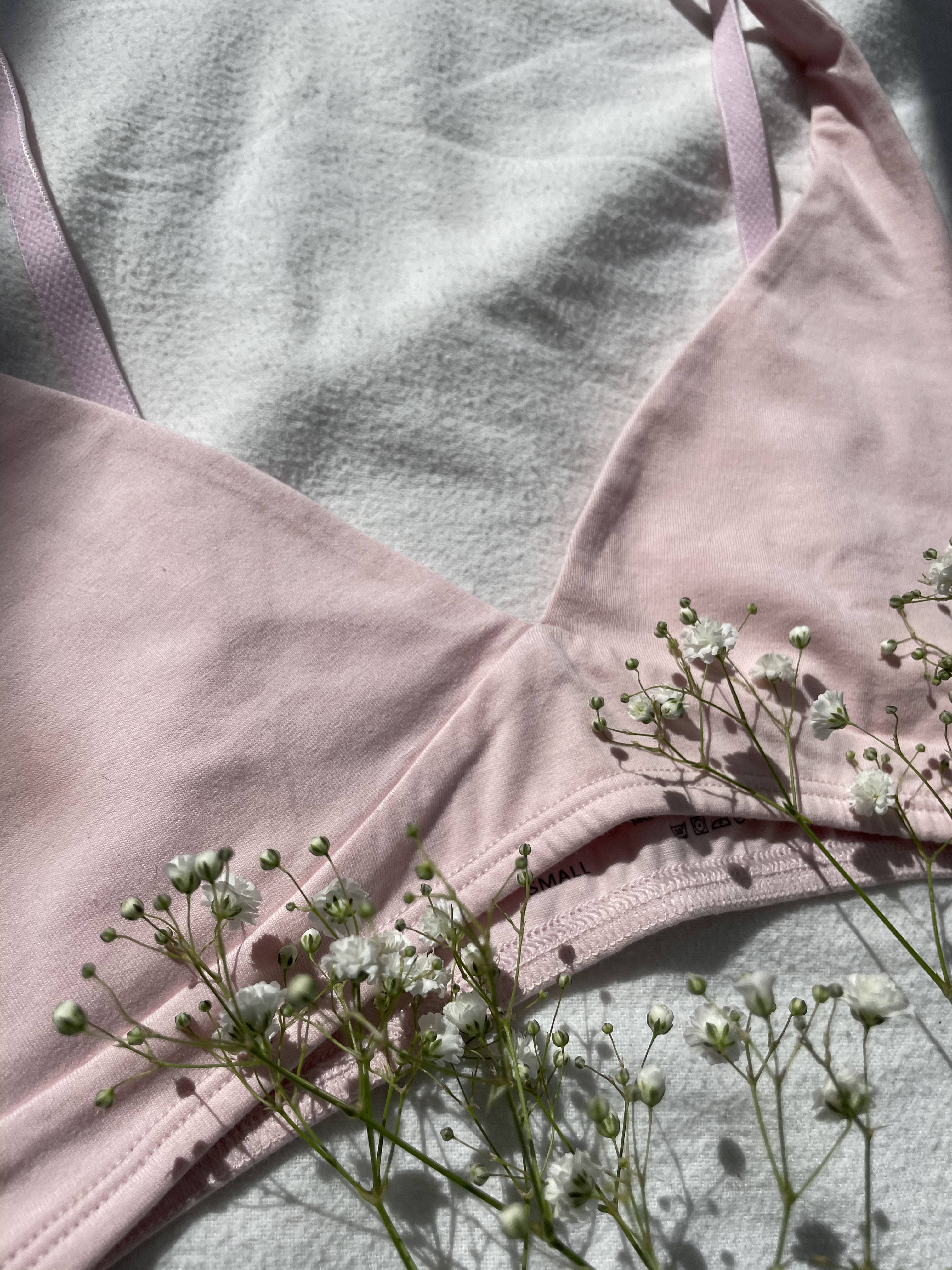 Light pink bralette on a white sheet with white flowers.