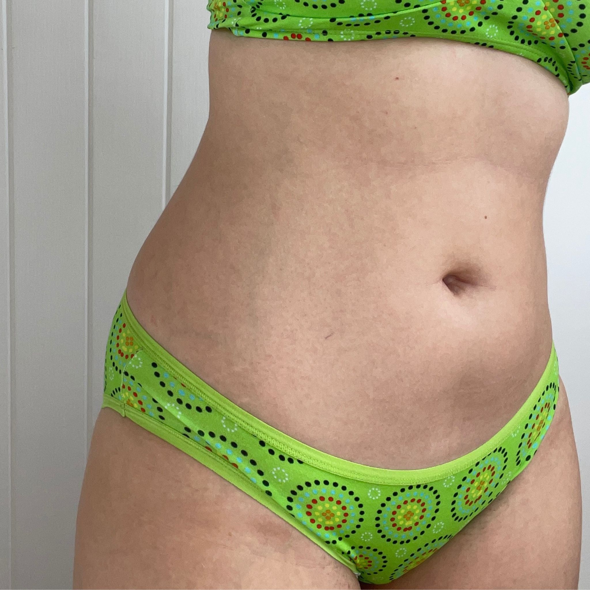 Person wearing green bikini bottoms and bralette with circular patterns, standing indoors
