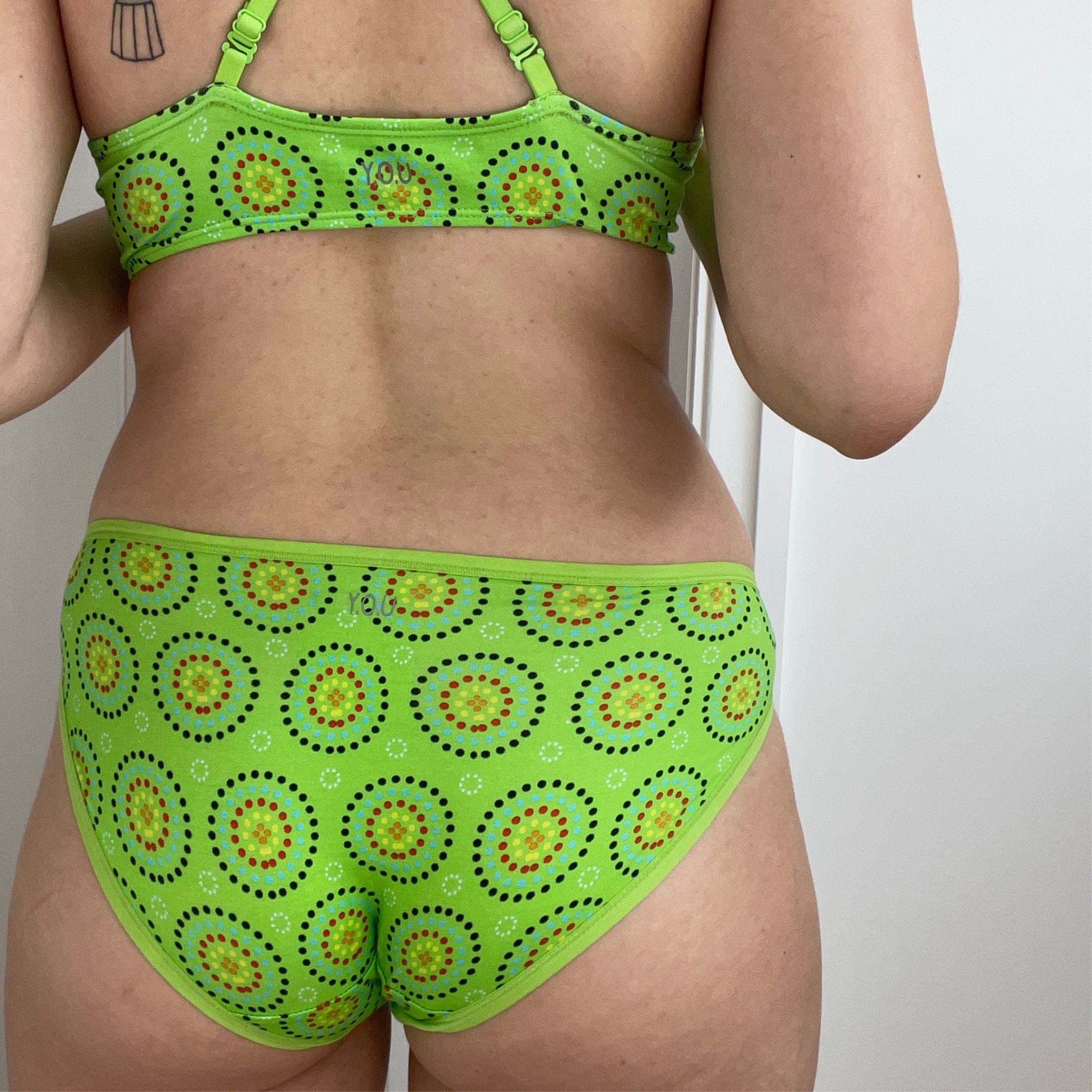 Person wearing green bikini bottoms and bralette with circular patterns, standing indoors